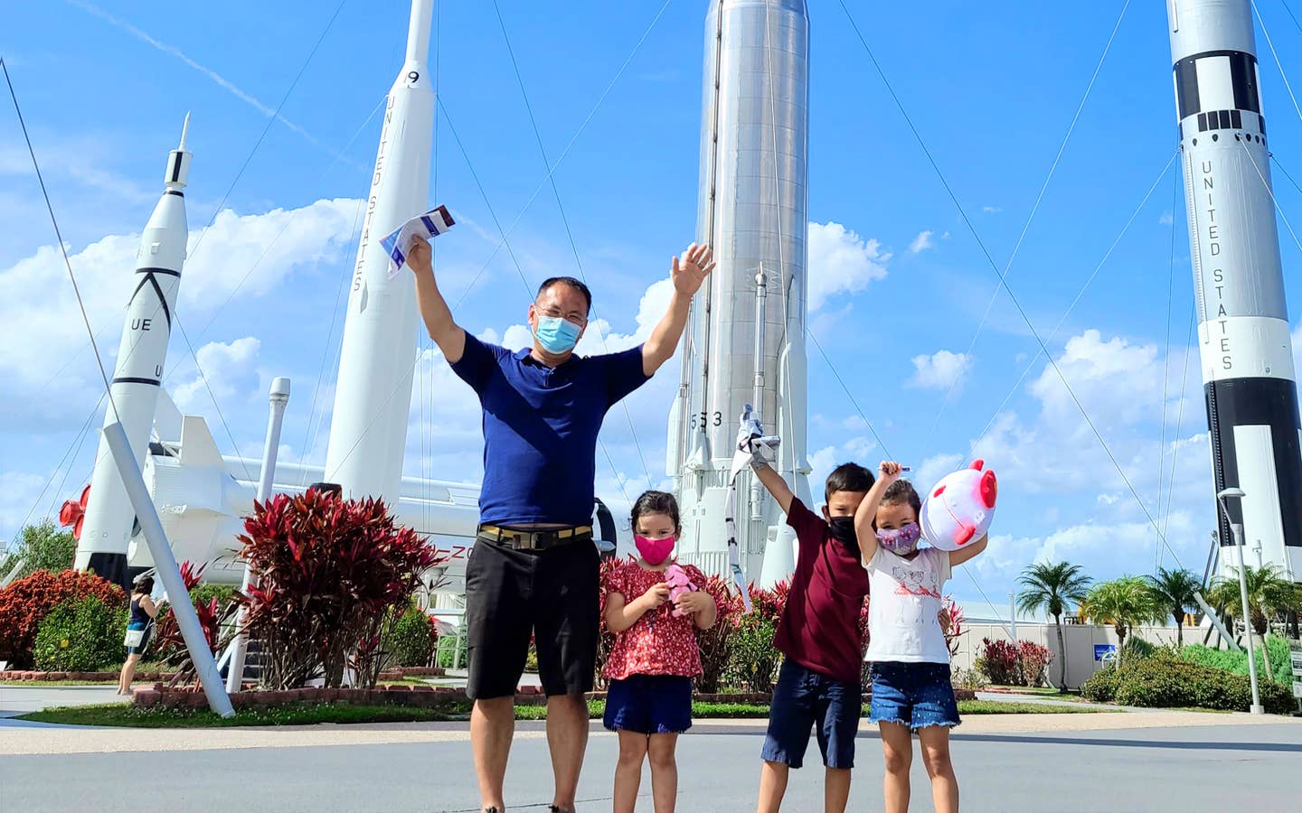 Featured Contributor, Angelica Kajiwara's husband and three children run pose in front of a 'Rocket Playground' located at the Kennedy Space Center™ Visitor Complex.