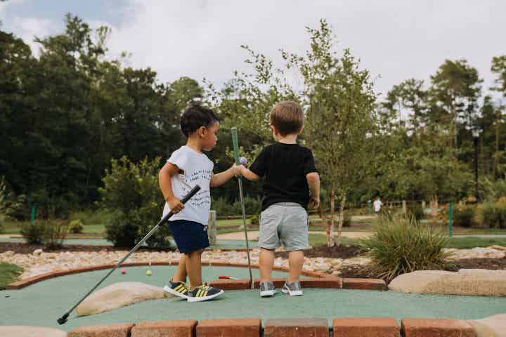 Two toddlers holding golf clubs at a mini golf course at Williamsburg Resort