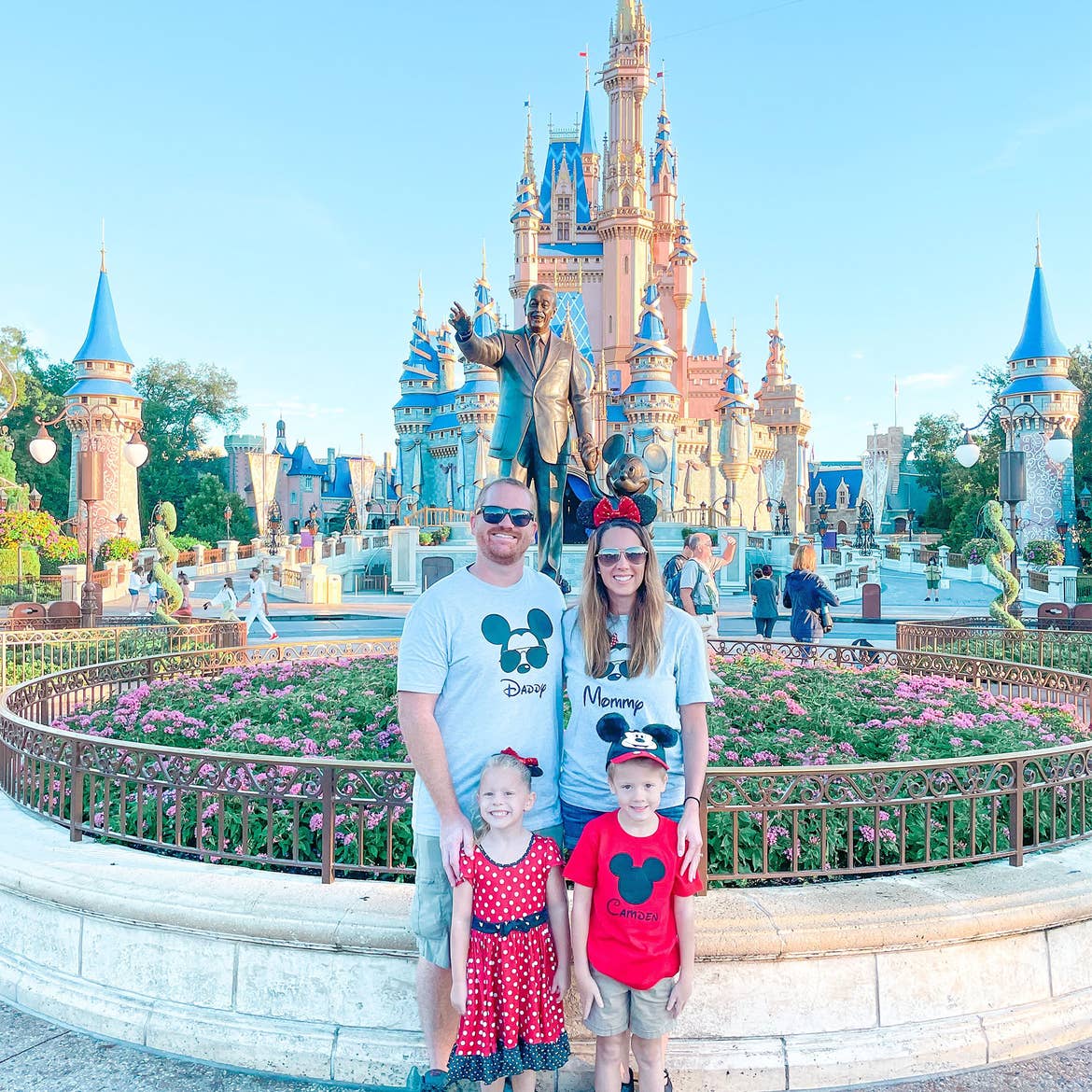 A man, woman, boy and girl stand wearing Disney apparel in front of Cinderella's Castle in Walt Disney World.