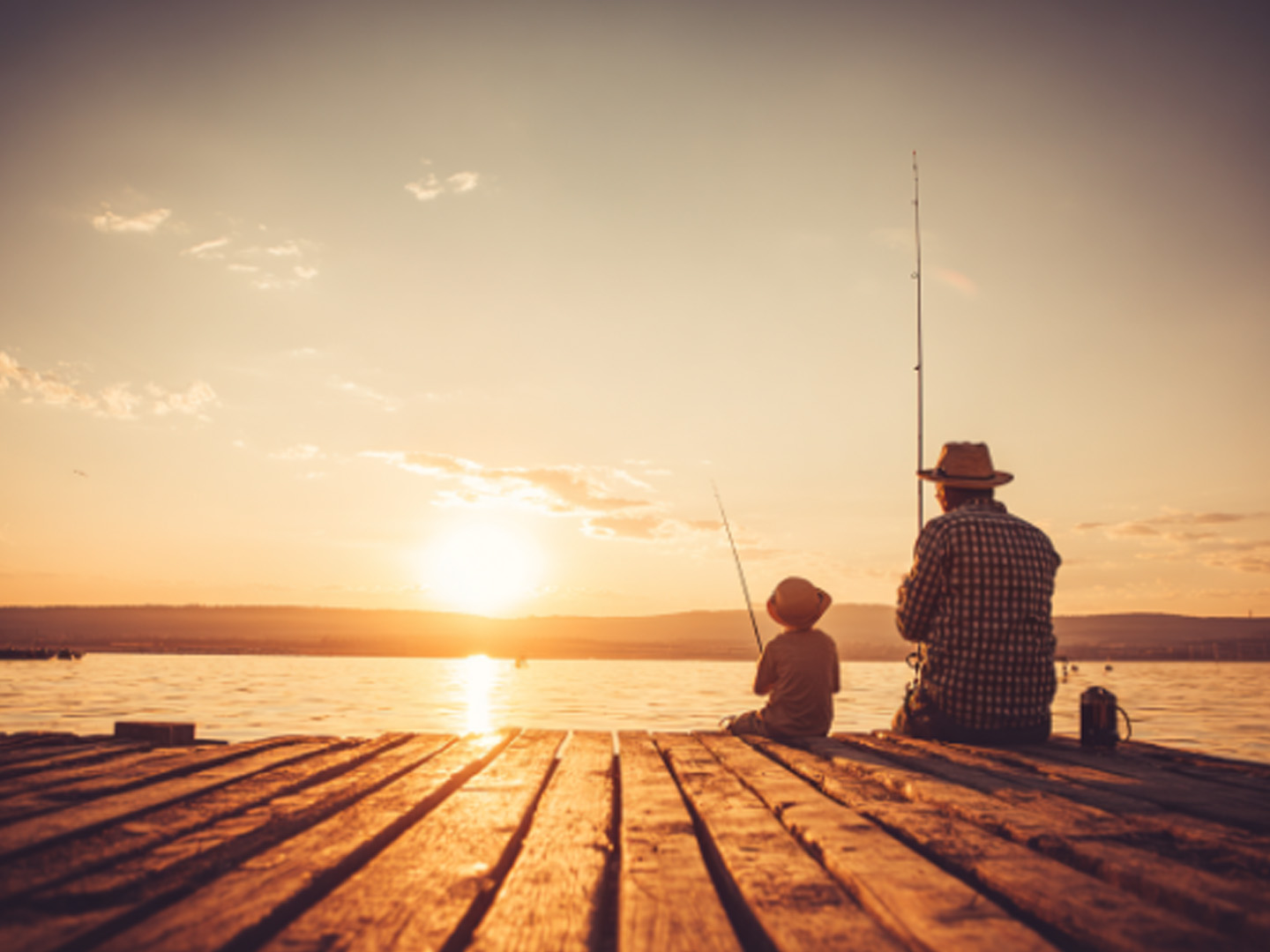 Sunset photo of father and son fishing on a dock.