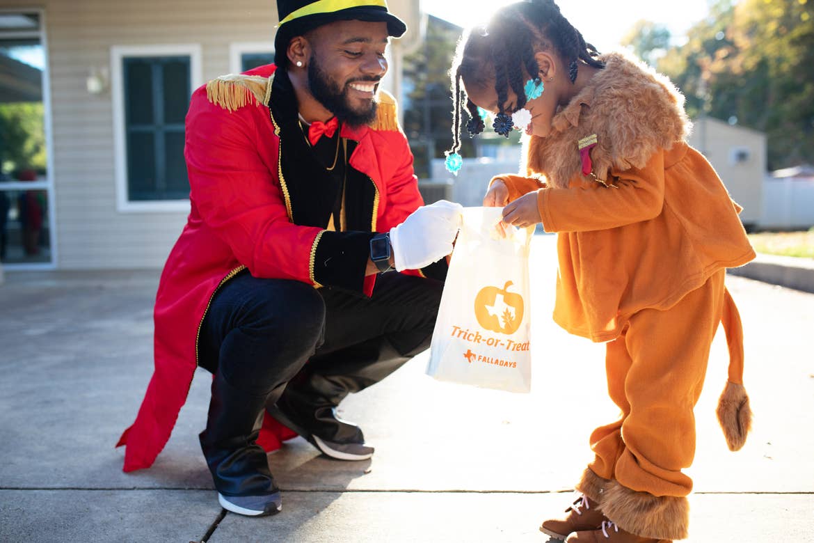 A man and young girl wear Halloween costumes while holding a canvas bag of treats.