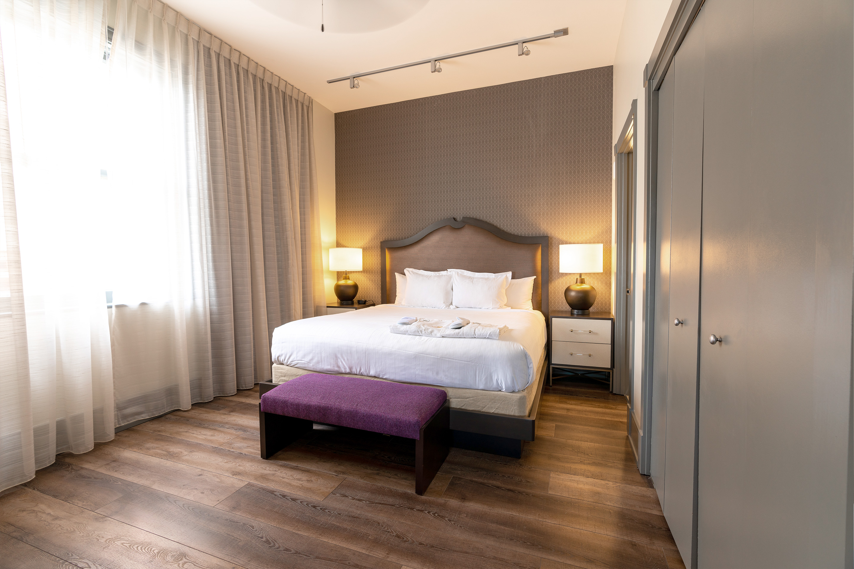 King bed with a purple bedroom bench and a closet in a one-bedroom Signature Collection villa at New Orleans Resort in Louisiana.