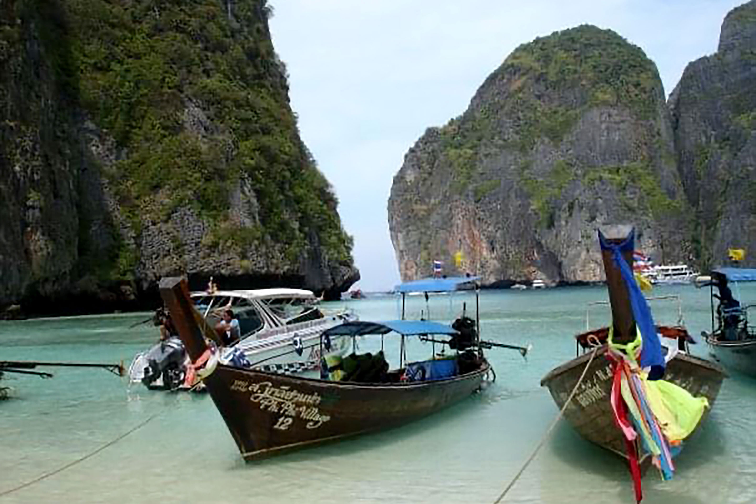 Several docked wooden boats on a beach near an ocean and cliffside rock formations.