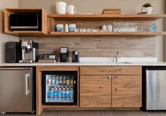 Well-equipped hotel kitchenette featuring wooden cabinetry, open shelving, and stocked mini-fridge.