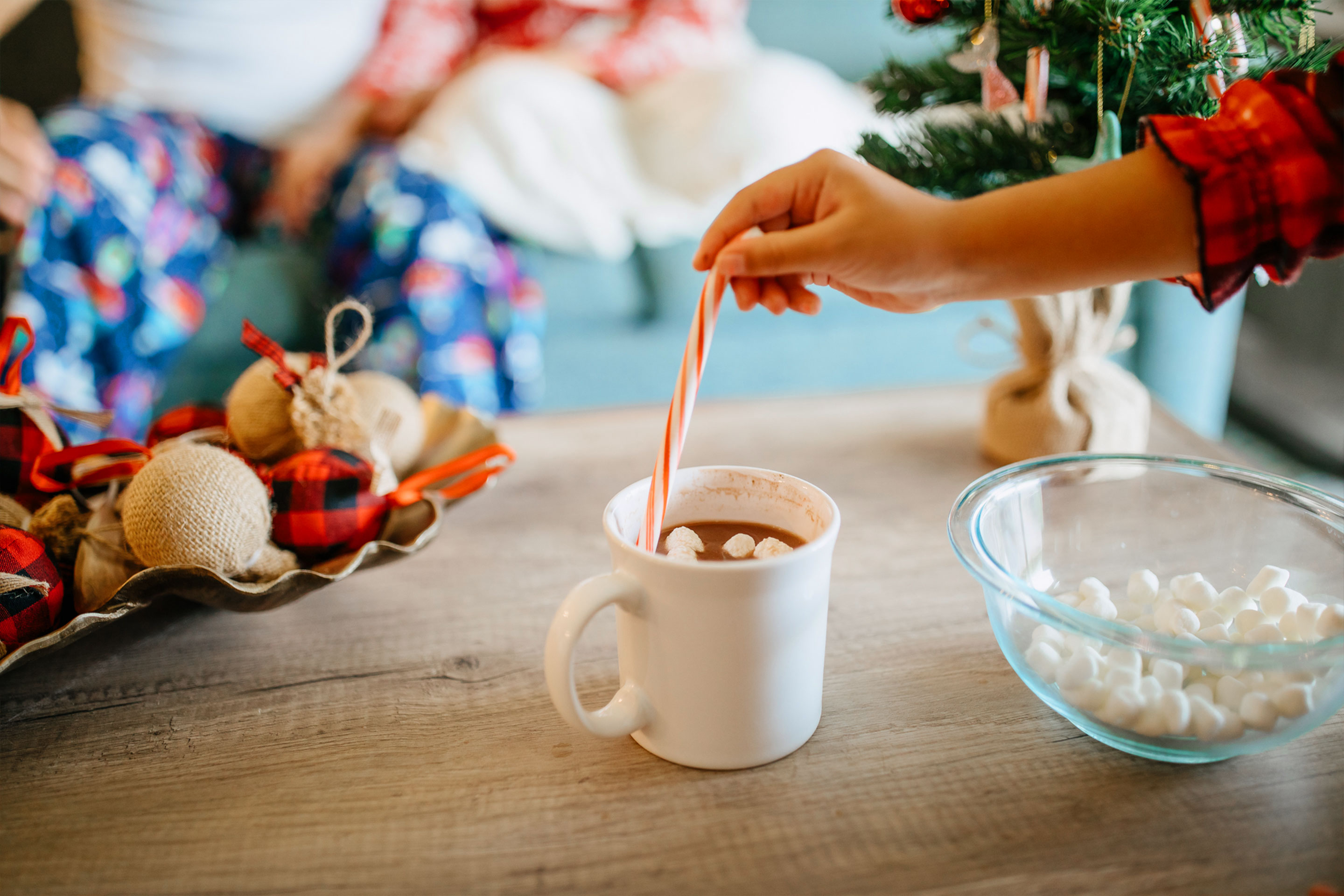 a girls hand stirs hot cocoa in a white mug with a candy cane.