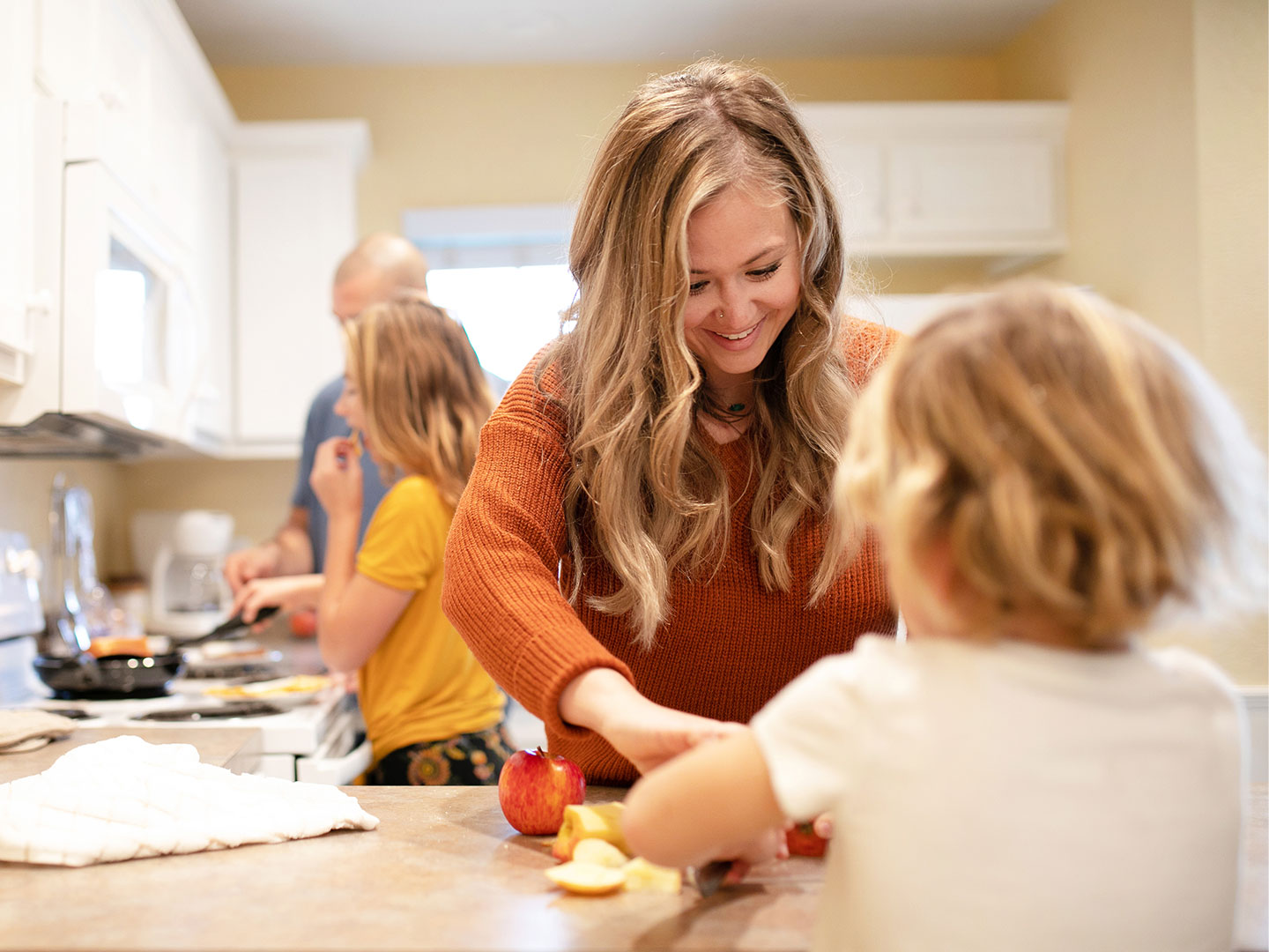 A woman in an orange sweater (front-right) helps serve a meal her husband and daughter (back-left) prepared in their Villa kitchen.