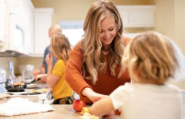 A woman in an orange sweater (front-right) helps serve a meal her husband and daughter (back-left) prepared in their Villa kitchen.