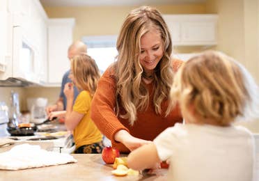 A woman in an orange sweater (front-right) helps serve a meal her husband and daughter (back-left) prepared in their Villa kitchen.