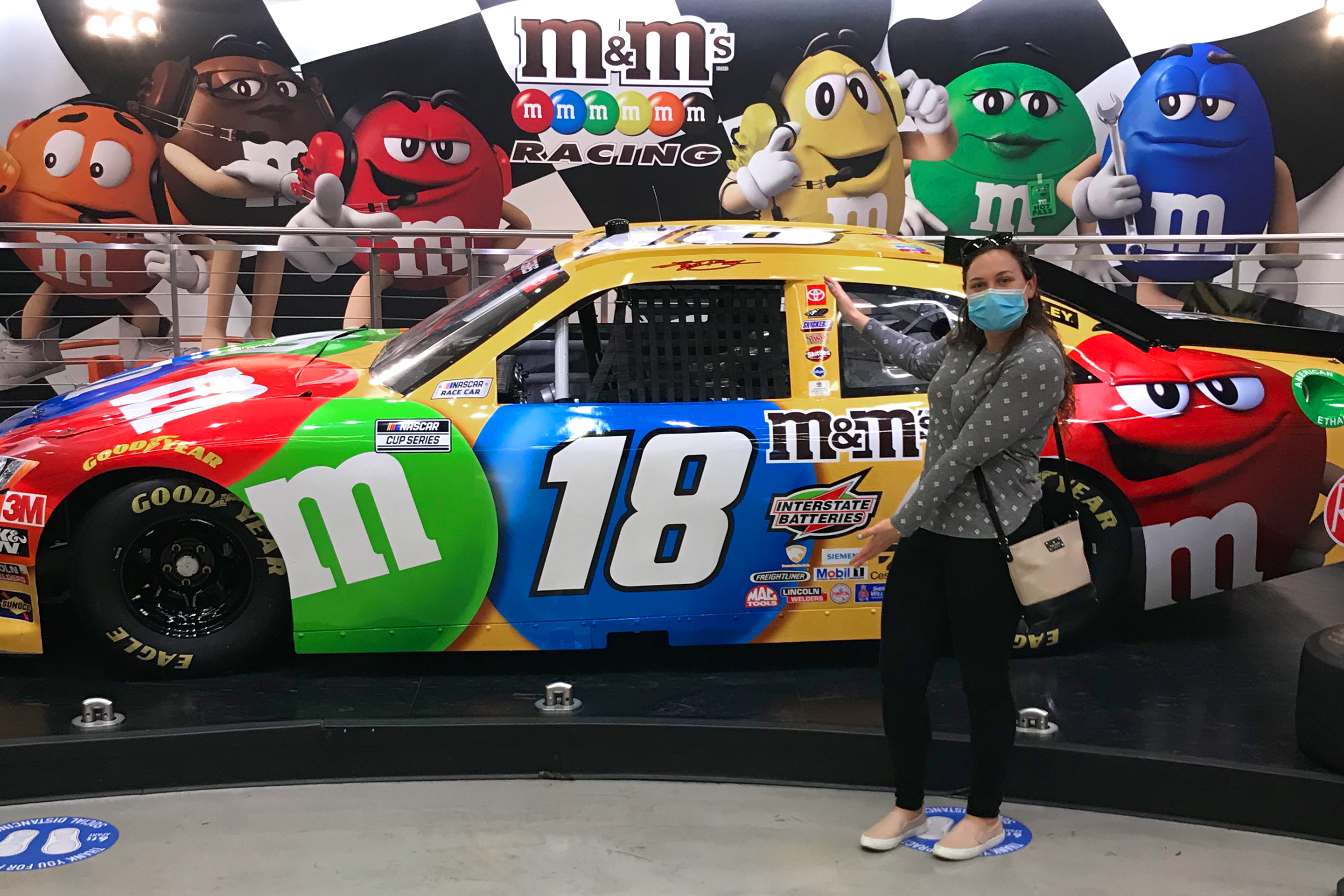Featured Contributor, Ashley Fraboni, stands in front of a race car with m&m decals.