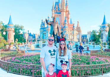 A man, woman, boy and girl stand wearing Disney apparel in front of Cinderella's Castle in Walt Disney World.