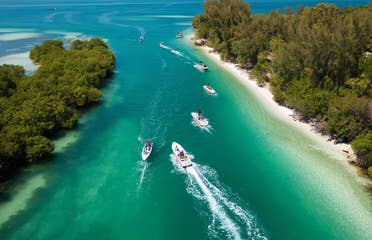 Drone view of boats in strait, gliding on aqua blue water and next to white sand.