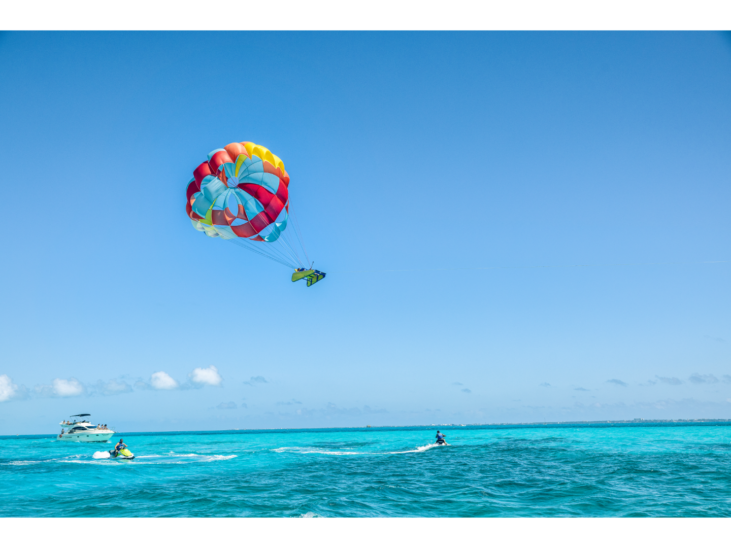 Colorful parasail pulls a person above turquoise ocean water.