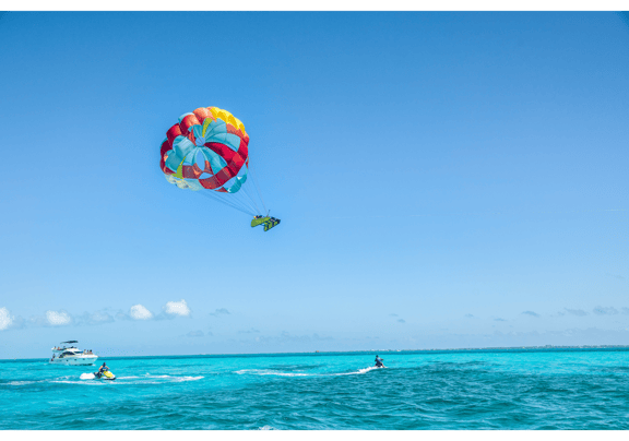 Colorful parasail pulls a person above turquoise ocean water.