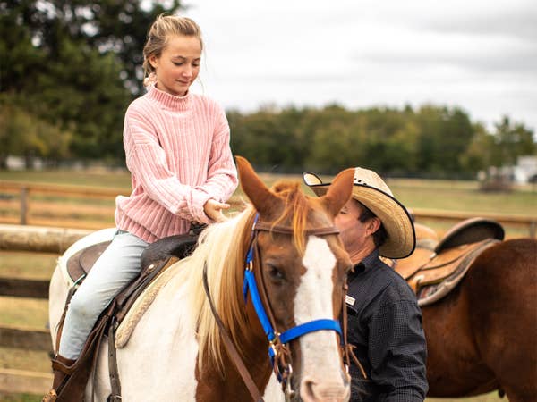 Child sitting on horse with adult supervising at Villages Resort in Flint, Texas.
