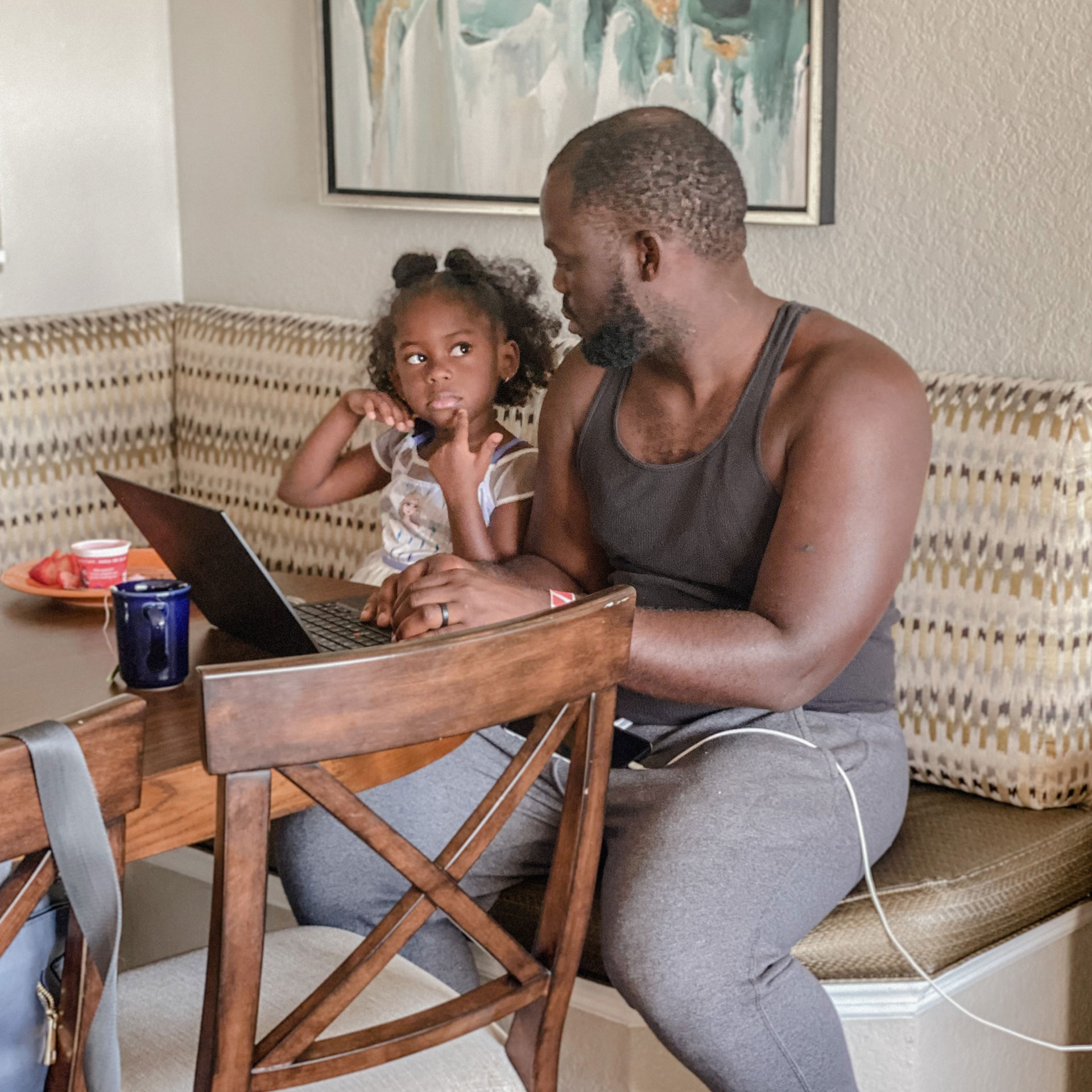 Author, Kimberly Gelin's daughter (left), sits on her dad's (right) lap at the dining table in our Villa at Orange Lake Resort in Florida with her laptop for virtual learning.