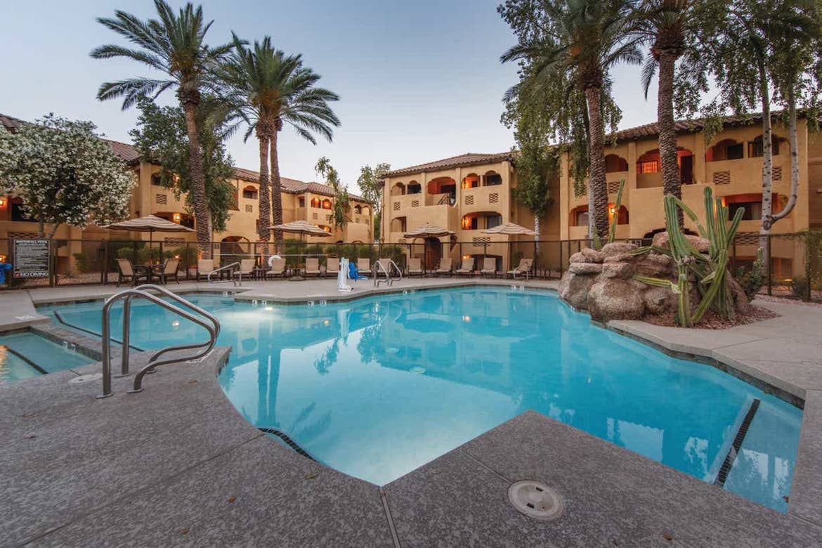 A view of the pool at Scottsdale Resort with villa buildings and palm trees in the background.