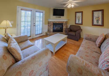 Living room with two couches, an accent chair, flat screen TV, and fireplace in a presidential two bedroom villa at Piney Shores Resort in Conroe, Texas