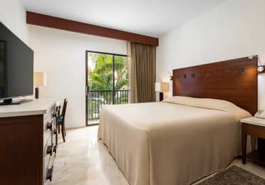 Suite bedroom with king bed and balcony overlooking gardens.