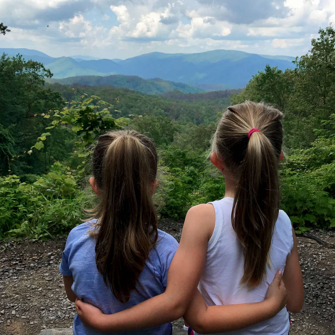 Author, Chris Johnstons' daughters, Kyndall (right), and Kyler (left) face out to the trees of the Great Smoky Mountains while wrapping one arm around each other.
