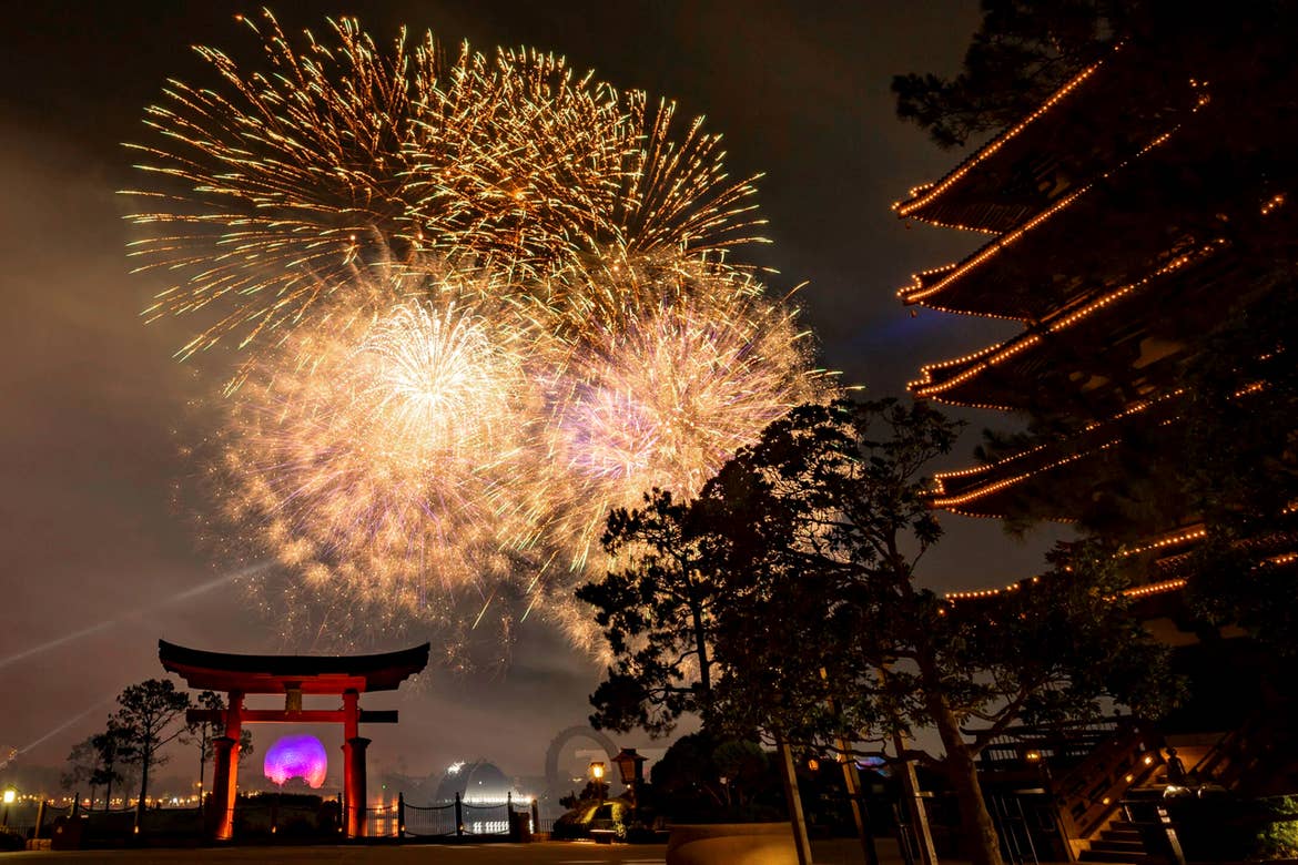 Fireworks explode in the air at night near the Epcot Japan Pavillion surrounded by a red Torii Gate and structure.
