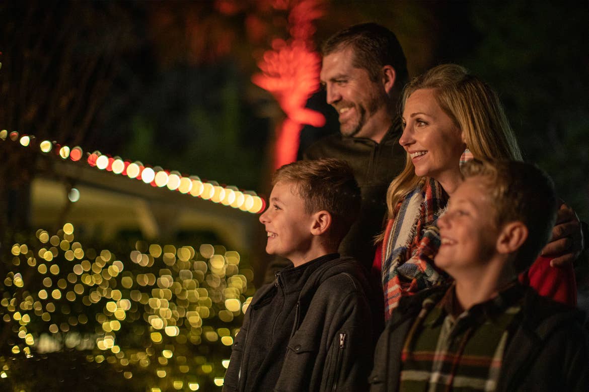 A man, woman and two young boys stand outdoors looking at red and white christmas lights.