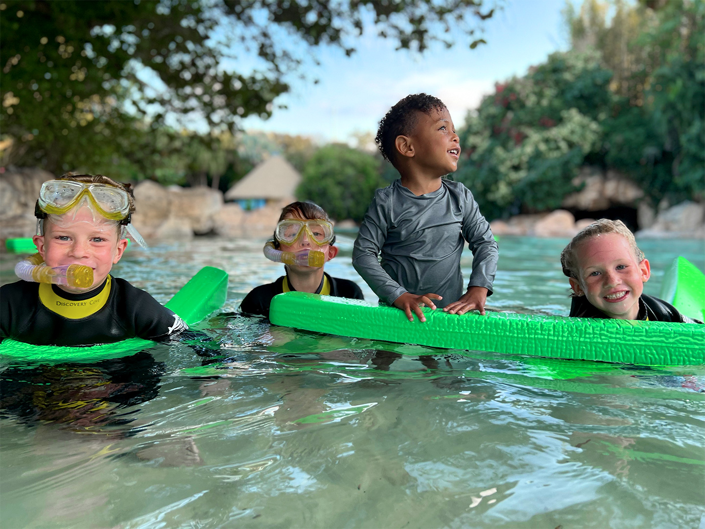Four kids wear swimwear and snorkel gear while wading in water outdoors.