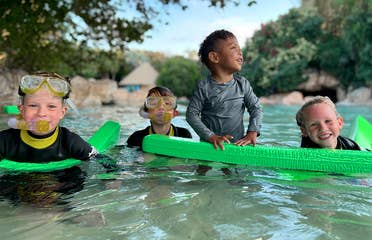 Four kids wear swimwear and snorkel gear while wading in water outdoors.
