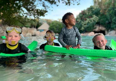 Four kids wear swimwear and snorkel gear while wading in water outdoors.