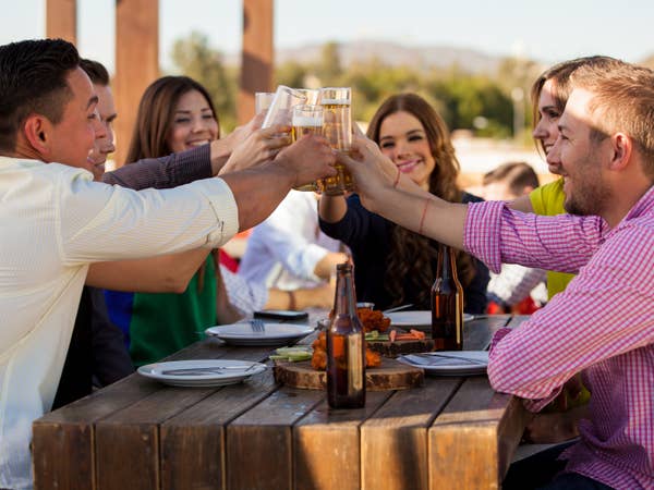 Group of young people toasting with glasses of white wine while dining outdoors