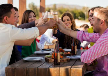 Group of young people toasting with glasses of white wine while dining outdoors
