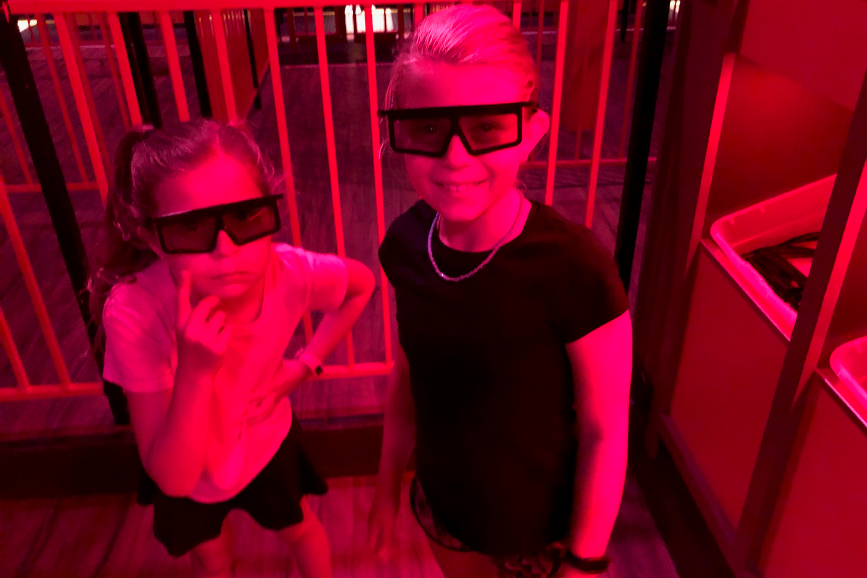 Two young girls stand in a queue wearing 3D glasses.