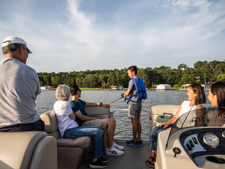 Family of six sitting on pontoon boat while child fishes at Villages Resort in Flint, Texas.