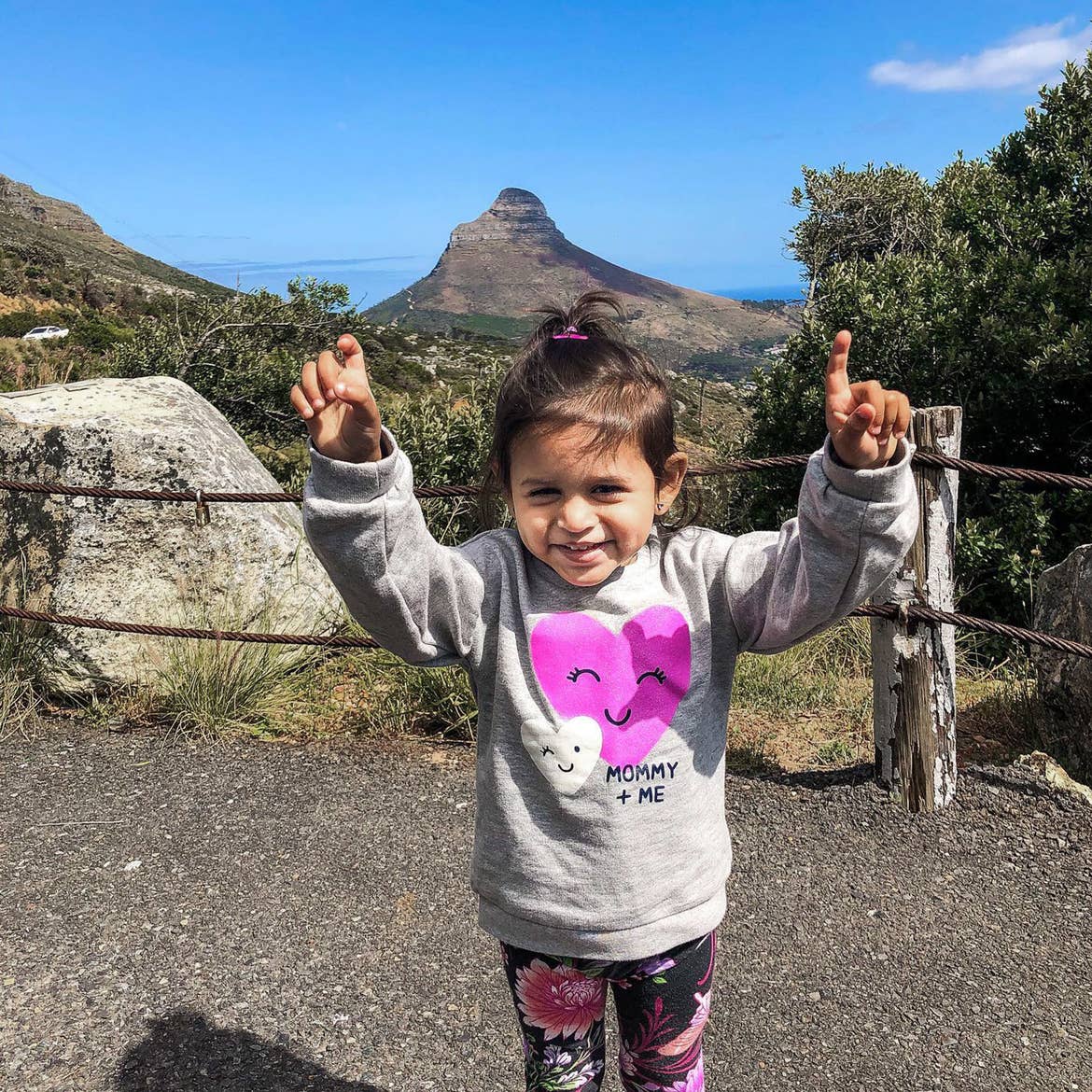 Featured Contributor, Karishma Kittur's daughter holds her fists up in the air as she accomplished climbing up a trail