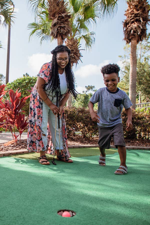 Mother and son playing mini golf outside surrounded by palm trees at Orange Lake Resort near Orlando, Florida.