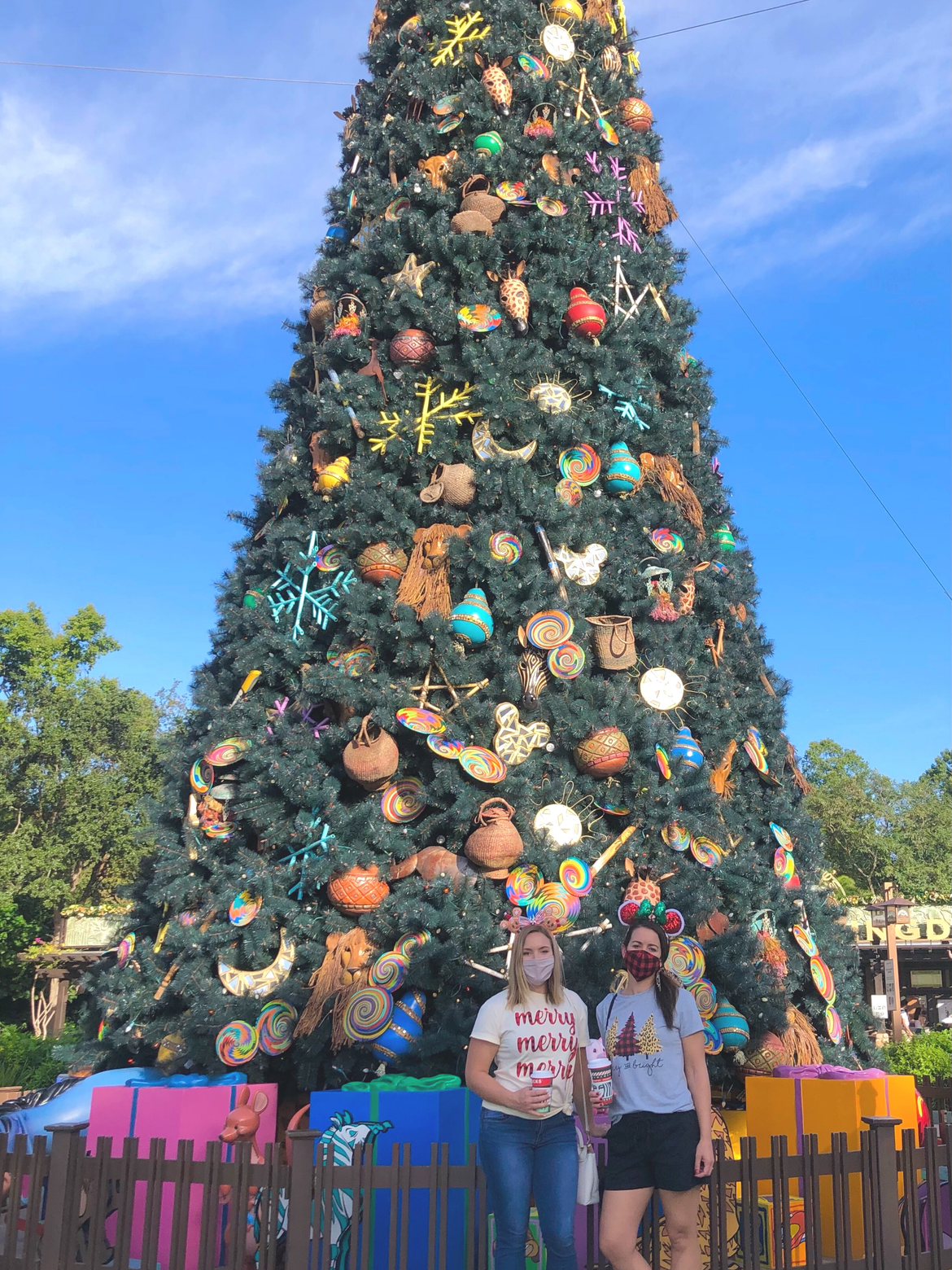 Author, Kelly Nelson (left), and Jenn C. Harmon (right) wear holiday inspired shirts and Minnie Mouse Ears within front of the Christmas Tree at Disney's Animal Kingdom Theme Park at Walt Disney World® Resort.