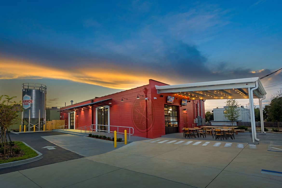 A multicolored cinderblock building exterior with fermenter decal that reads, 'Ivanhoe Park Brewing Co.' as the sun sets in the distance.