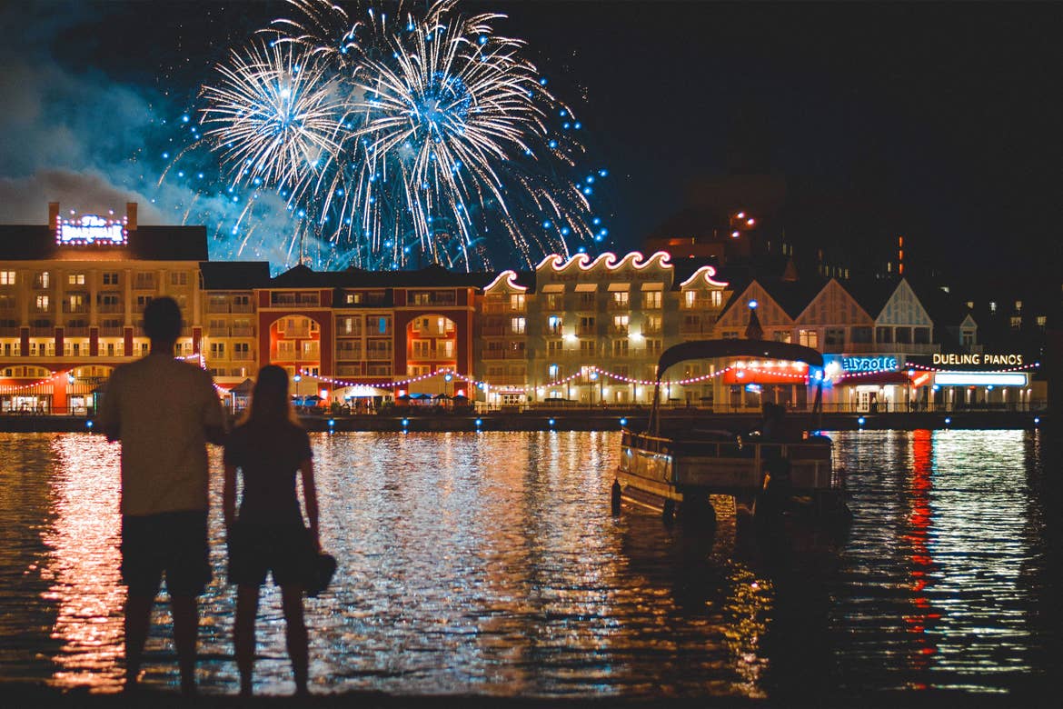 A man and woman (left) stand watching fireworks at night overlooking the Disney Boardwalk.