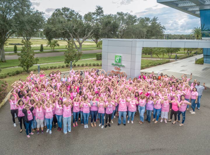 Large group of people all waring pink and making heart shapes with their hands towards the camera and Holiday Inn Club Vacation's corporate headquarters.