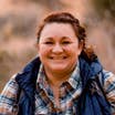Featured Contributor, Melody Forsyth, stands outdoors wearing a blue vest and flannel shirt.