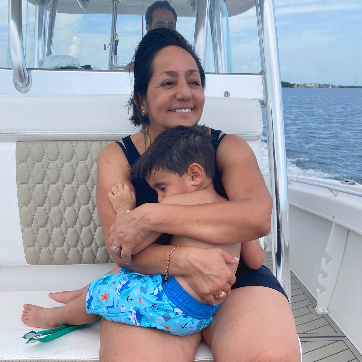 A woman holds a sleeping toddler while a man drives a boat that they are seated on.