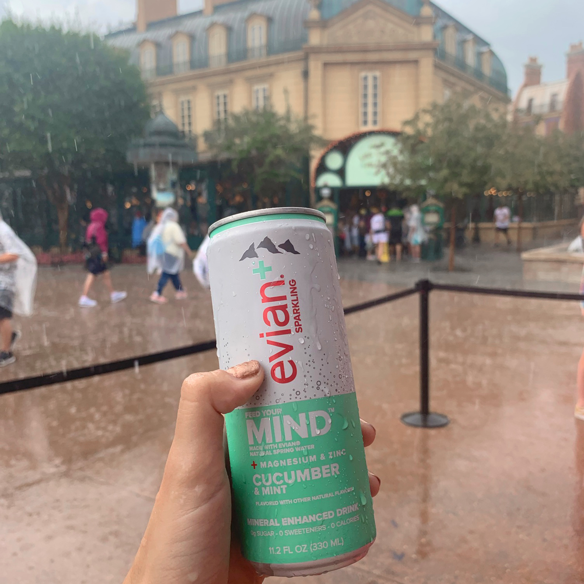 A hand holds an aluminum can of Evian near the France Pavilion at Epcot in the rain.