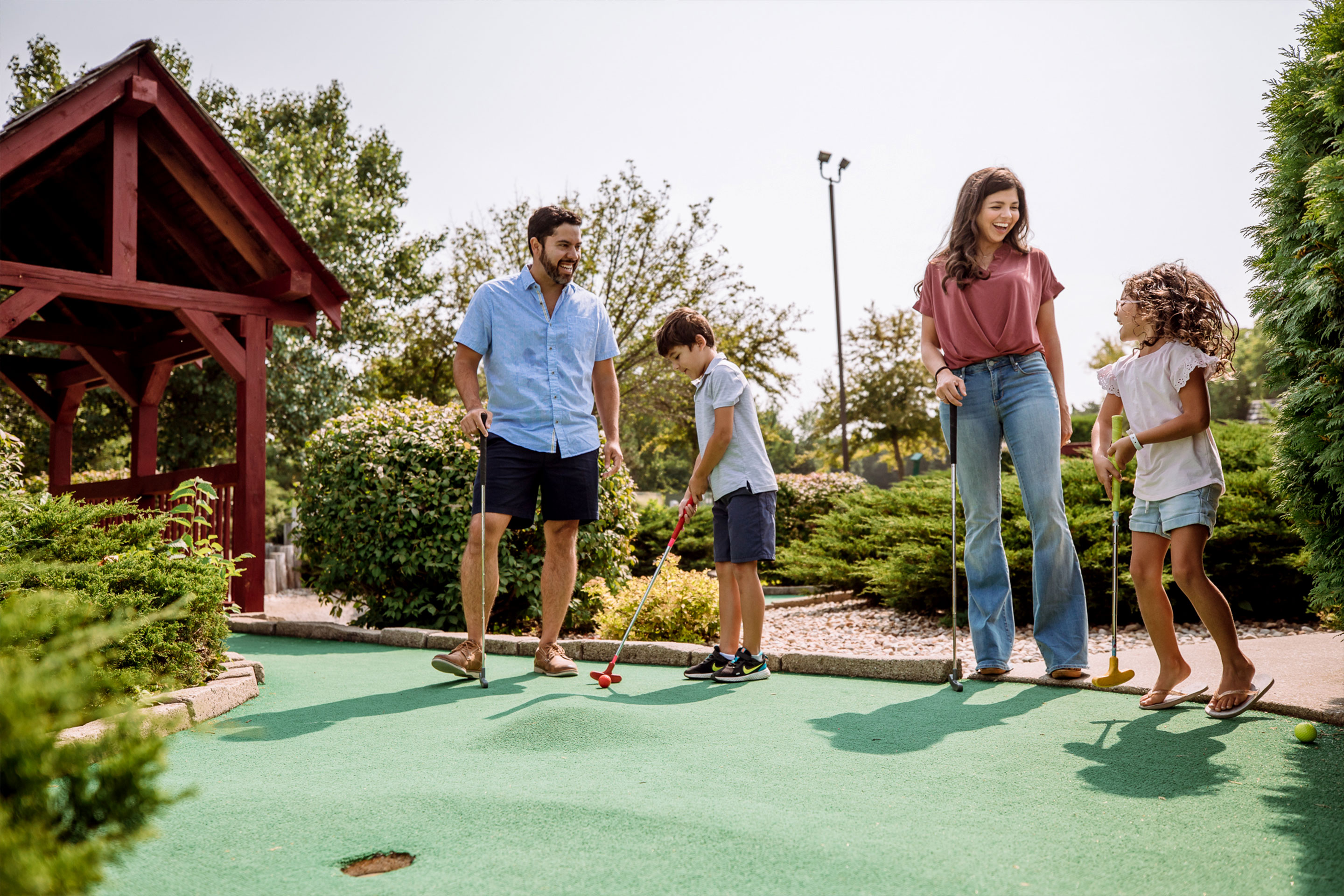 from left to right: A man, a young boy, a woman and a young girl play mini golf outdoors.