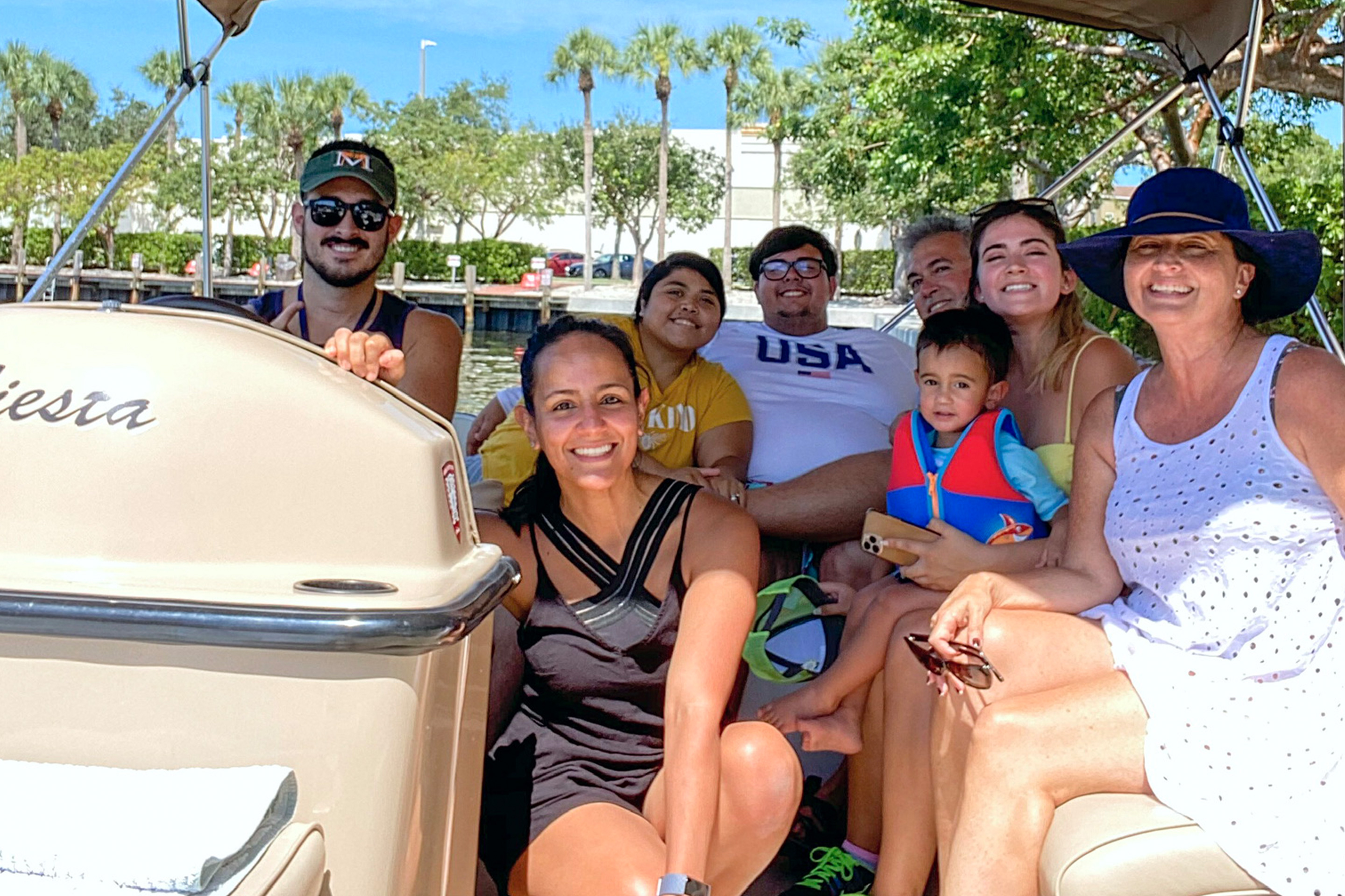 Featured Contributor, Danny Pitaluga (left) wears sunglasses, a blue tank and a hat behind the steering wheel while his wife and their extended family sit on a boat.