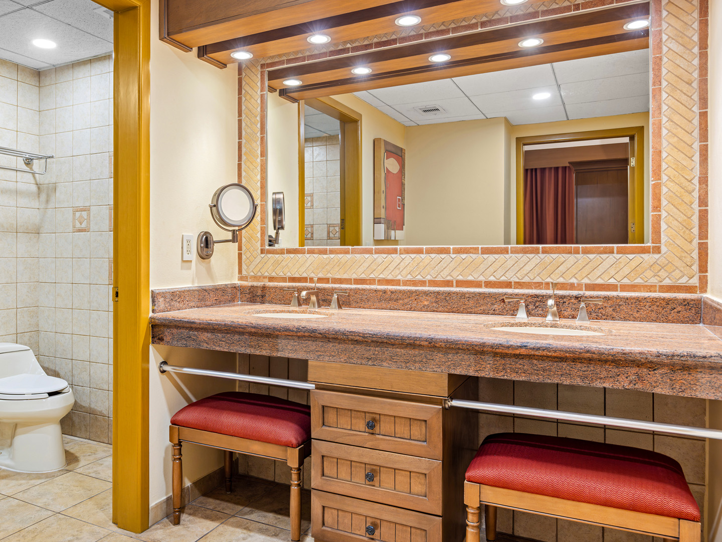 Bathroom with granite double vanity, seating, and tiled walls.