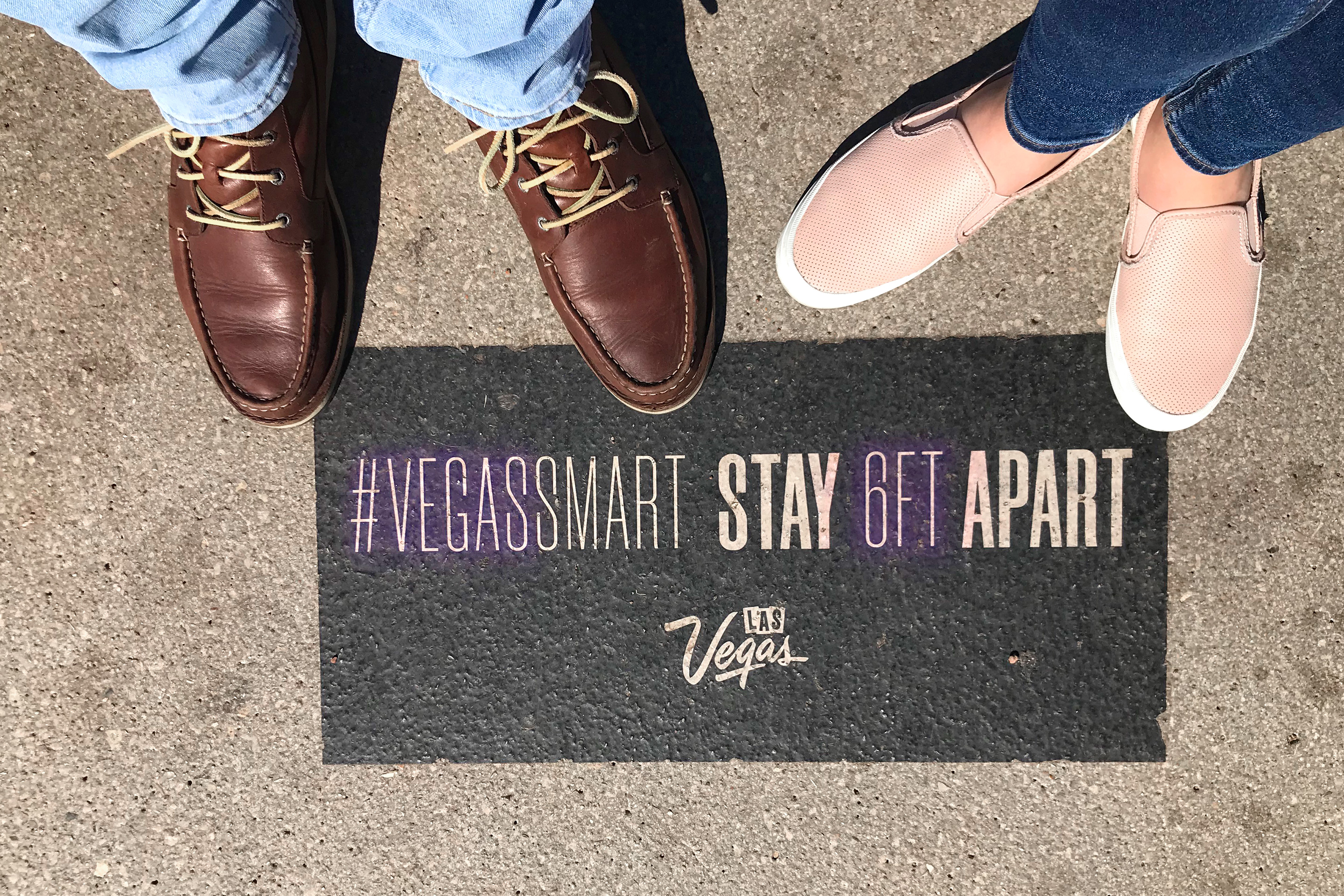 Featured Contributor, Ashley Fraboni (right) and her fiancé (left) stand on a marker that indicates social distancing that reads, '#VegasSmart Stay 6 FT. Apart.'