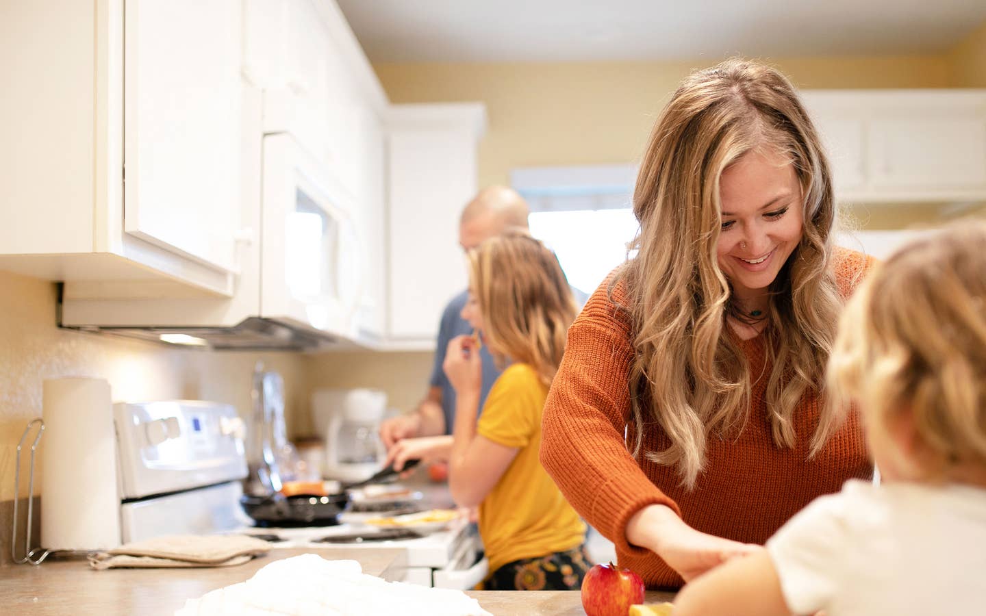 A woman in an orange sweater (front-right) helps serve a meal her husband and daughter (back-left) prepared in their Villa kitchen.