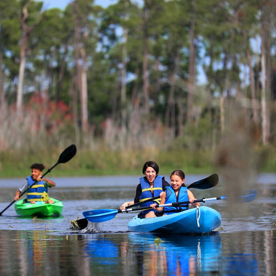 Featured Contributor, Clarissa Laskey (middle), kayaks with her daughter (right) in a blue kayak while her son (left) kayaks in his own green kayak.