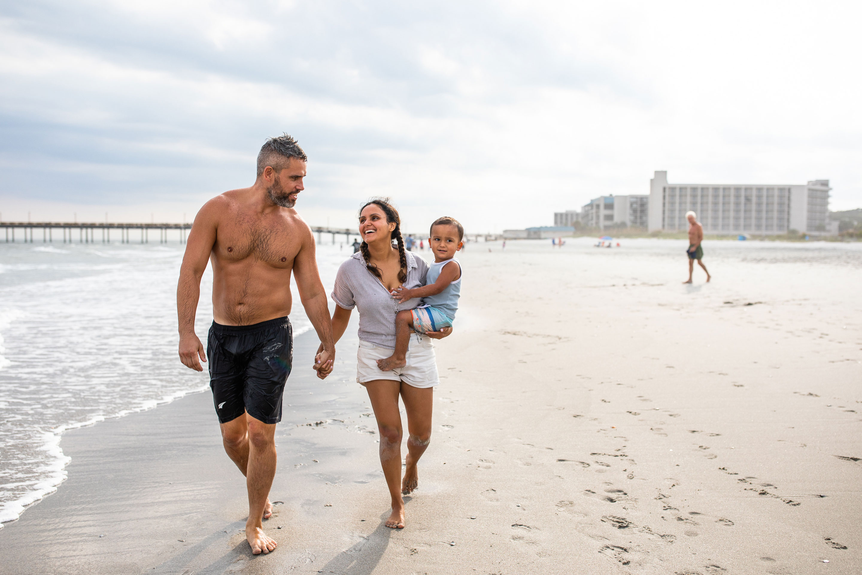 Author, Brenda Rivera Stearns (right), and husband, Isaiah (left), walk along the sandy beach while toting her son.