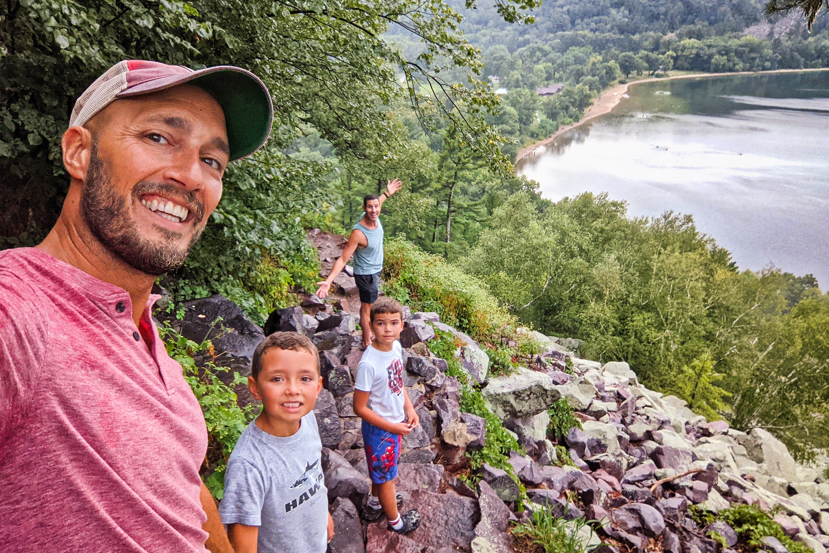 A family of two men and two boys overlook a river from a cliff.