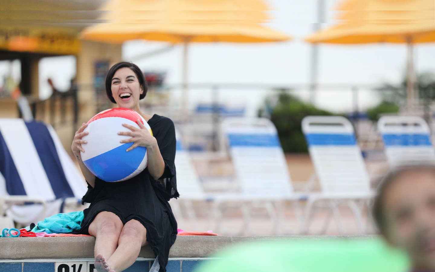 Woman holding beach ball while sitting poolside.